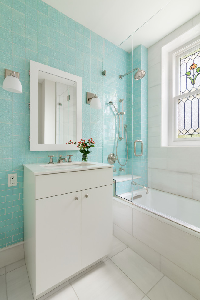 This is an example of a mid-sized contemporary 3/4 bathroom in New York with flat-panel cabinets, white cabinets, an alcove tub, a shower/bathtub combo, blue tile, ceramic tile, an undermount sink, white floor, a hinged shower door and white benchtops.