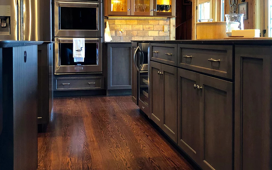 Large mountain style u-shaped dark wood floor and brown floor eat-in kitchen photo in Boston with an undermount sink, recessed-panel cabinets, gray cabinets, soapstone countertops, beige backsplash, travertine backsplash, stainless steel appliances, two islands and black countertops