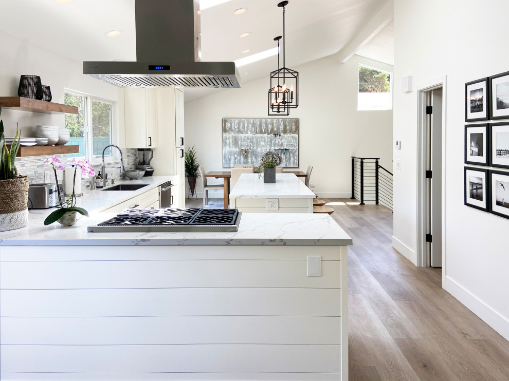 Mid-sized transitional l-shaped vinyl floor, brown floor and vaulted ceiling eat-in kitchen photo with an undermount sink, shaker cabinets, white cabinets, quartz countertops, multicolored backsplash, mosaic tile backsplash, stainless steel appliances, an island and white countertops