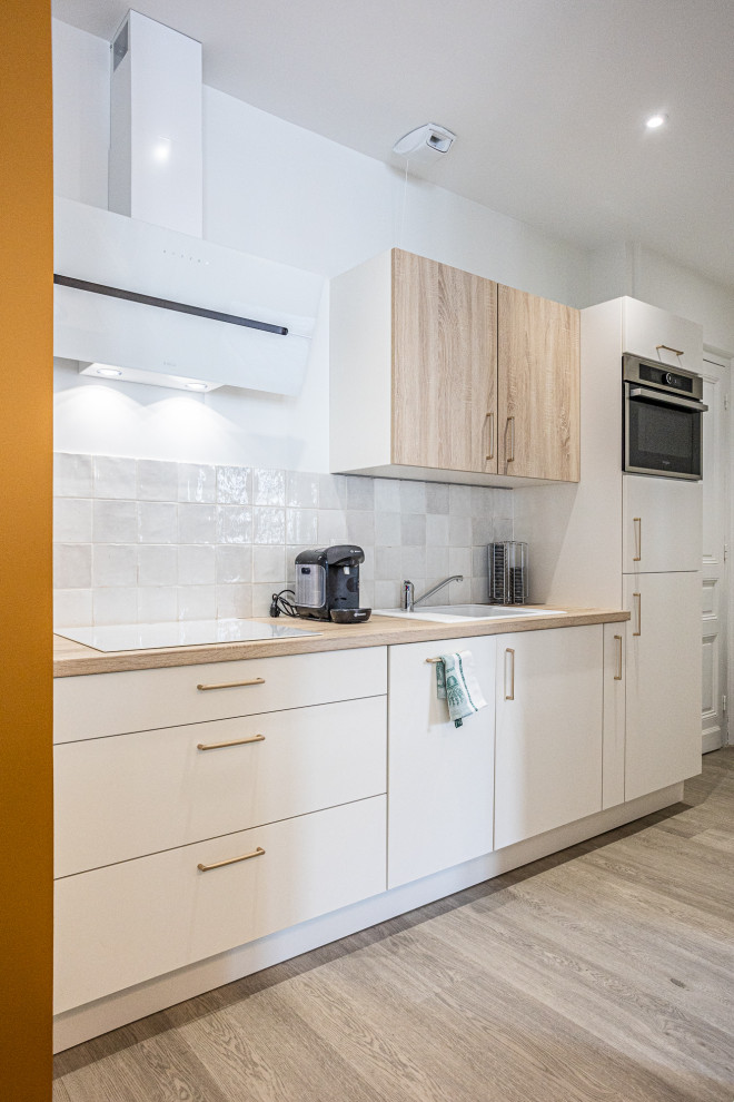 Bild på ett litet minimalistiskt linjärt kök med öppen planlösning, med en nedsänkt diskho, beige skåp, träbänkskiva, vitt stänkskydd, stänkskydd i terrakottakakel, rostfria vitvaror och ljust trägolv