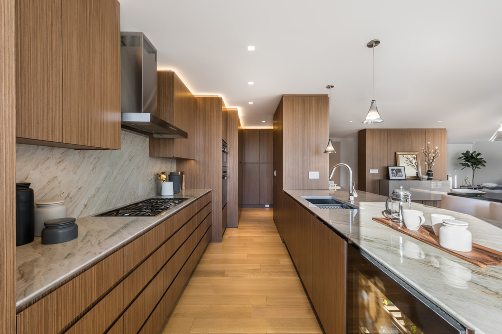 Inspiration for a large contemporary galley kitchen in New York with flat-panel cabinets, medium wood cabinets, multi-coloured splashback, multi-coloured benchtop, quartzite benchtops, stone slab splashback, panelled appliances, light hardwood floors, with island and a double-bowl sink.