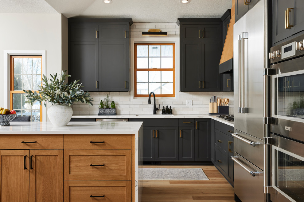 Eat-in kitchen - large transitional l-shaped vinyl floor and brown floor eat-in kitchen idea in Minneapolis with an undermount sink, shaker cabinets, black cabinets, quartz countertops, white backsplash, porcelain backsplash, stainless steel appliances, an island and white countertops