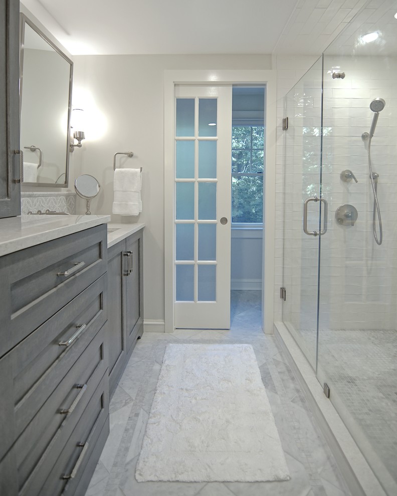 Design ideas for a mid-sized traditional master bathroom in Boston with recessed-panel cabinets, grey cabinets, a two-piece toilet, white tile, subway tile, grey walls, marble floors, an undermount sink, engineered quartz benchtops, grey floor and a hinged shower door.