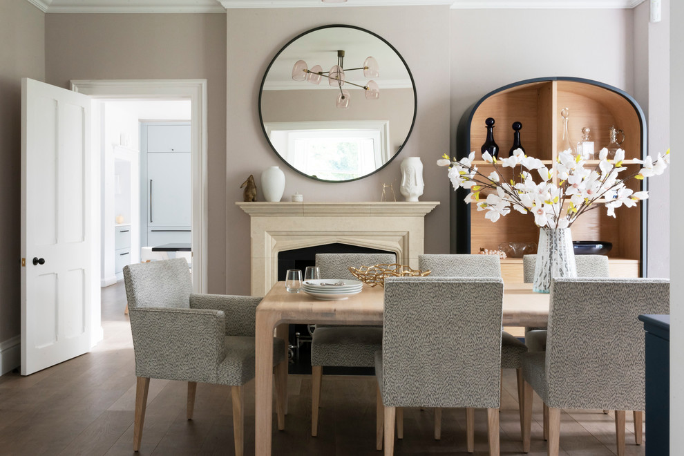 Inspiration for a transitional separate dining room in London with medium hardwood floors, a standard fireplace, a stone fireplace surround, brown floor and beige walls.