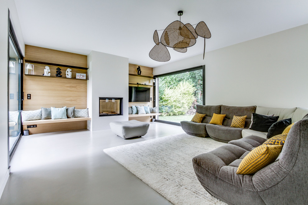 This is an example of an expansive contemporary open concept family room in Paris with beige walls, concrete floors, a two-sided fireplace, a plaster fireplace surround, a wall-mounted tv, grey floor and wood walls.