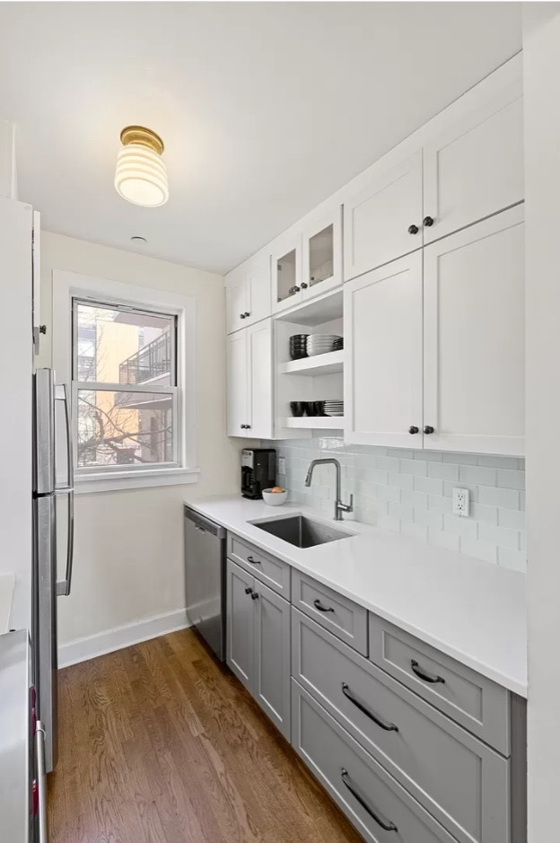 Inspiration for a small transitional galley separate kitchen in New York with an undermount sink, shaker cabinets, white cabinets, quartz benchtops, grey splashback, glass tile splashback, stainless steel appliances, medium hardwood floors, no island, brown floor and white benchtop.