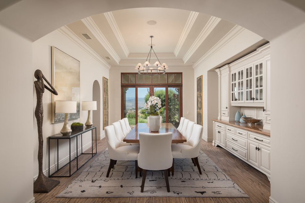 This is an example of a mediterranean dining room in Los Angeles with white walls, medium hardwood floors and brown floor.