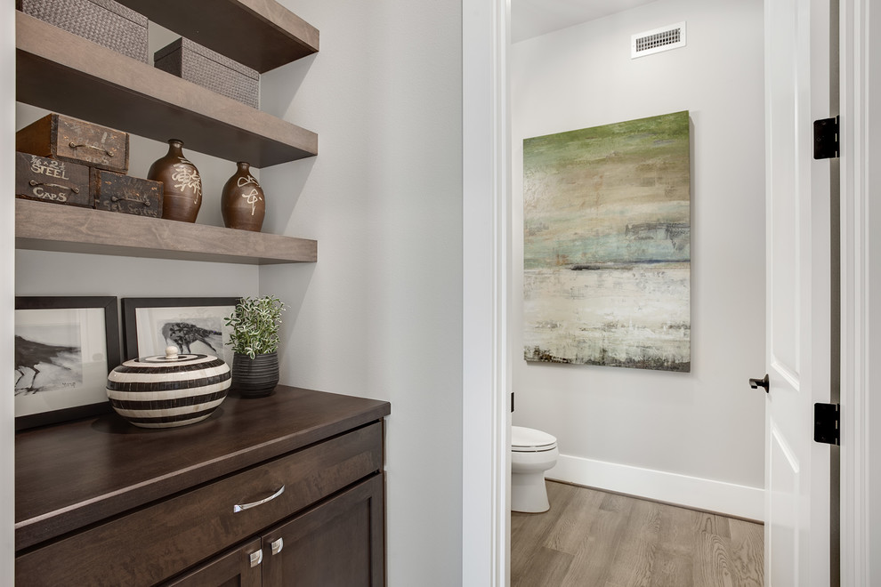 Photo of a mid-sized transitional powder room in Seattle with recessed-panel cabinets, dark wood cabinets, a two-piece toilet, grey walls, light hardwood floors, wood benchtops, grey floor and brown benchtops.