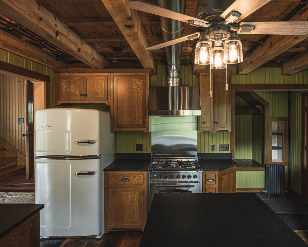 Example of a mountain style medium tone wood floor and exposed beam kitchen design with an undermount sink, shaker cabinets, granite countertops, black backsplash, granite backsplash, stainless steel appliances, an island and black countertops