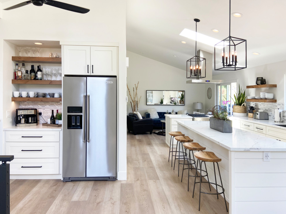 Inspiration for a mid-sized transitional l-shaped vinyl floor, brown floor and vaulted ceiling eat-in kitchen remodel with an undermount sink, shaker cabinets, white cabinets, quartz countertops, multicolored backsplash, mosaic tile backsplash, stainless steel appliances, an island and white countertops