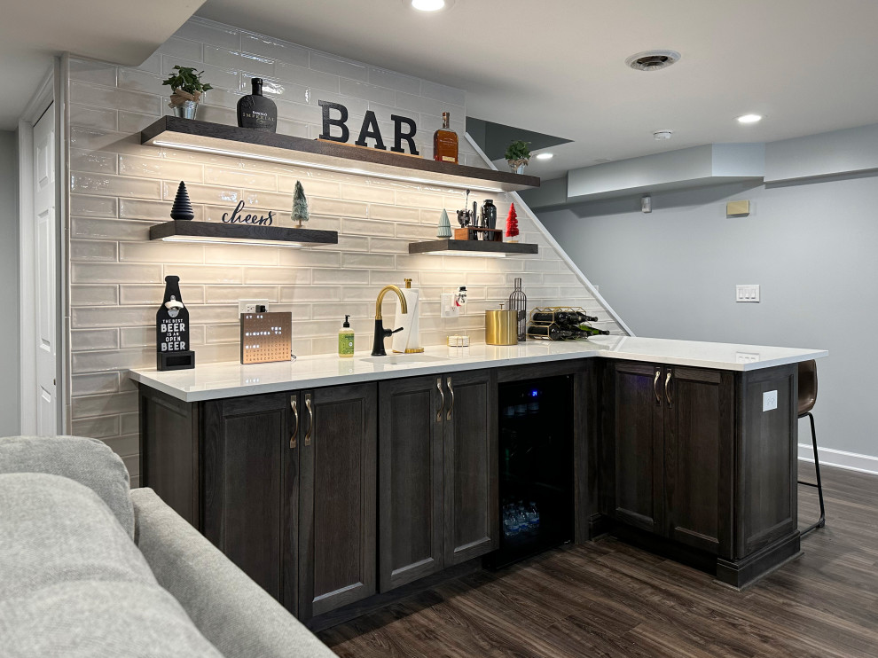 Design ideas for a mid-sized transitional l-shaped wet bar in Chicago with an undermount sink, shaker cabinets, brown cabinets, white splashback, subway tile splashback, vinyl floors, brown floor and white benchtop.