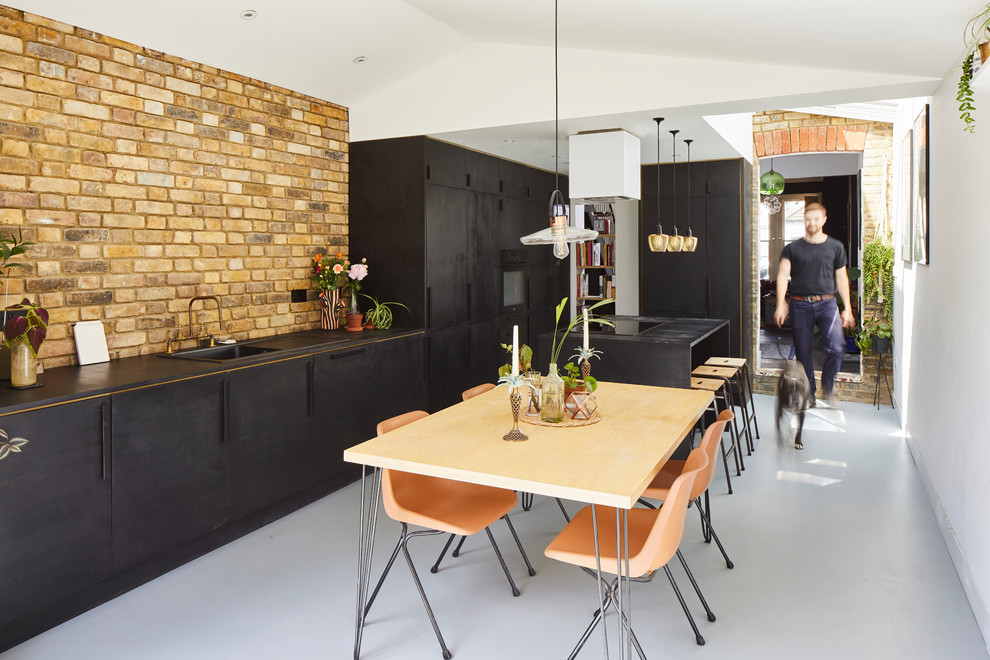 Contemporary galley eat-in kitchen in London with a drop-in sink, flat-panel cabinets, black cabinets, brown splashback, brick splashback, with island, grey floor and black benchtop.