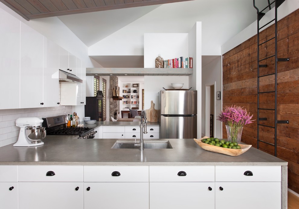 Inspiration for a contemporary u-shaped kitchen in Austin with flat-panel cabinets, white cabinets, concrete benchtops, white splashback, stainless steel appliances, an undermount sink, subway tile splashback, a peninsula and light hardwood floors.