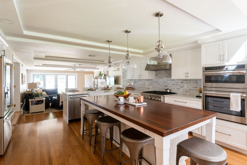 ボストンにある広いトランジショナルスタイルのおしゃれなキッチン (エプロンフロントシンク、シェーカースタイル扉のキャビネット、白いキャビネット、木材カウンター、白いキッチンパネル、レンガのキッチンパネル、シルバーの調理設備、無垢フローリング、茶色い床、茶色いキッチンカウンター、格子天井) の写真