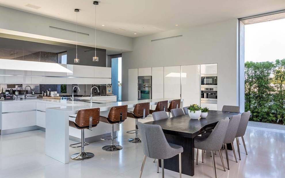 Eat-in kitchen - contemporary gray floor eat-in kitchen idea in Los Angeles with flat-panel cabinets, white cabinets, mirror backsplash, stainless steel appliances, a peninsula and gray countertops