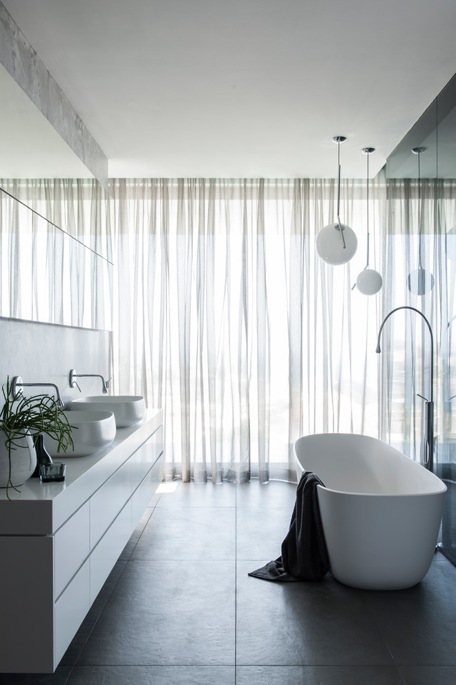 Photo of a large modern master bathroom in Sydney with furniture-like cabinets, white cabinets, a freestanding tub, an open shower, a wall-mount toilet, gray tile, marble, grey walls, porcelain floors, a vessel sink, solid surface benchtops, grey floor, an open shower and white benchtops.