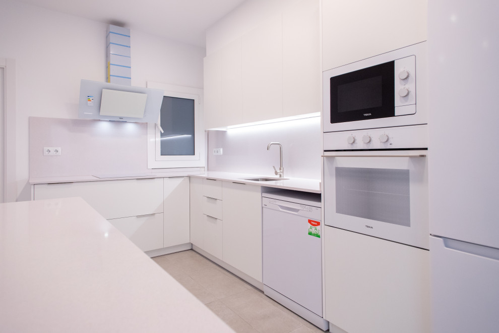 Large contemporary l-shaped open plan kitchen in Barcelona with a single-bowl sink, white cabinets, white splashback, white appliances, ceramic floors, no island, grey floor and white benchtop.