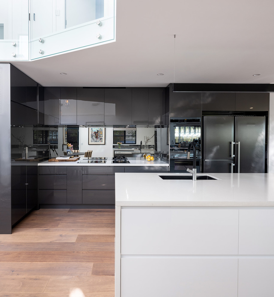 Inspiration for a contemporary galley kitchen in Sydney with an undermount sink, flat-panel cabinets, grey cabinets, mirror splashback, medium hardwood floors, with island, brown floor and white benchtop.