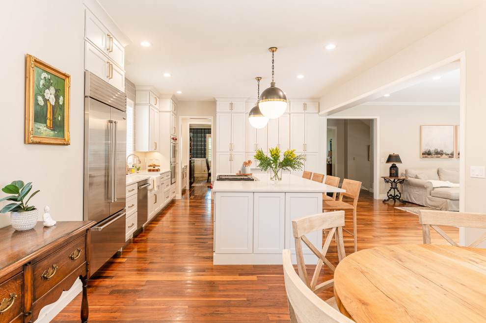 Example of a large transitional l-shaped dark wood floor and brown floor open concept kitchen design in Denver with a farmhouse sink, shaker cabinets, beige cabinets, quartz countertops, beige backsplash, ceramic backsplash, stainless steel appliances, an island and white countertops