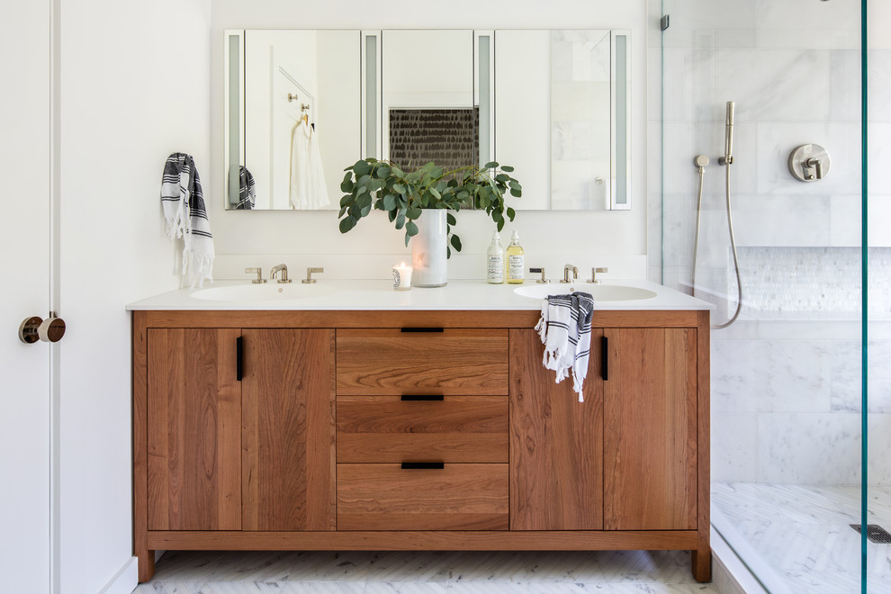 This is an example of a mid-sized transitional master bathroom in San Francisco with medium wood cabinets, white tile, stone tile, white walls, marble floors, an integrated sink, engineered quartz benchtops, white floor, white benchtops and flat-panel cabinets.