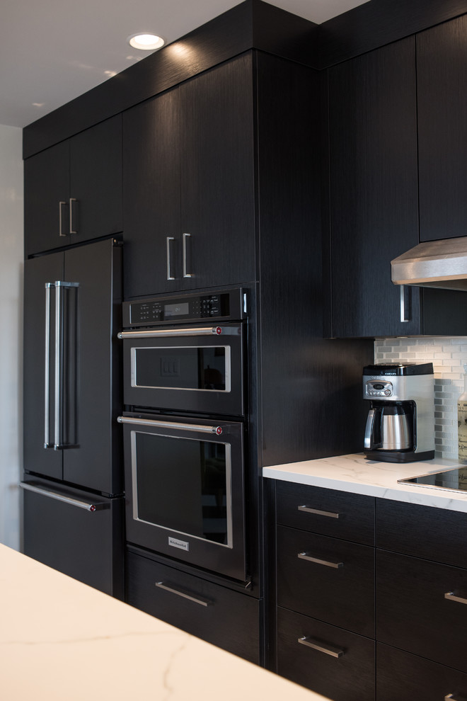 This is an example of a small contemporary u-shaped eat-in kitchen in Vancouver with an undermount sink, flat-panel cabinets, black cabinets, glass tile splashback, black appliances, vinyl floors and a peninsula.