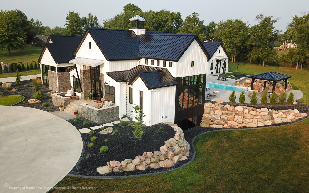 Foto della villa ampia bianca country a due piani con rivestimento in metallo, copertura in metallo o lamiera, tetto nero e pannelli e listelle di legno