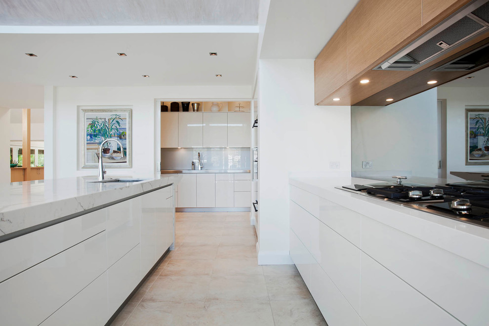 This is an example of a large modern l-shaped open plan kitchen in Sydney with an undermount sink, flat-panel cabinets, white cabinets, quartz benchtops, grey splashback, mirror splashback, black appliances, limestone floors and with island.