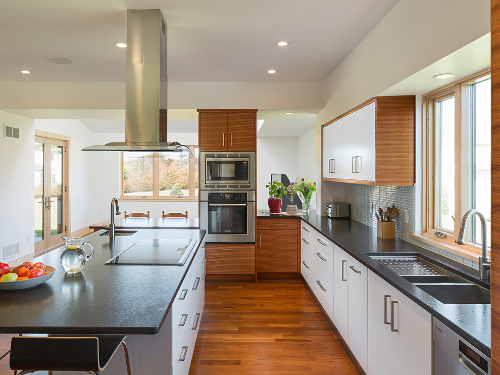 Inspiration for a modern l-shaped kitchen in Philadelphia with an undermount sink, flat-panel cabinets, white cabinets, granite benchtops, grey splashback, glass tile splashback, stainless steel appliances, light hardwood floors and with island.