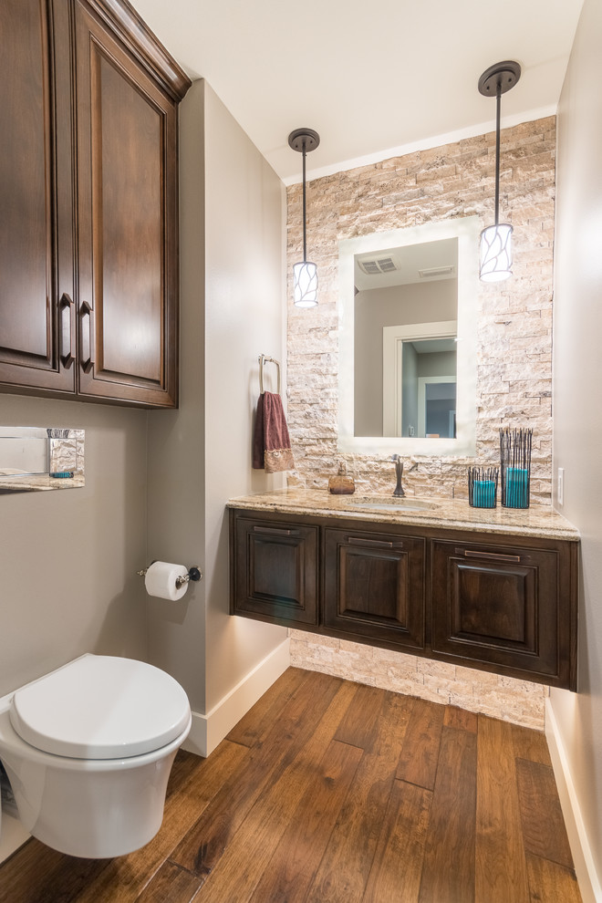 Small transitional powder room in Austin with raised-panel cabinets, dark wood cabinets, a wall-mount toilet, beige tile, stone tile, grey walls, medium hardwood floors, an undermount sink and granite benchtops.