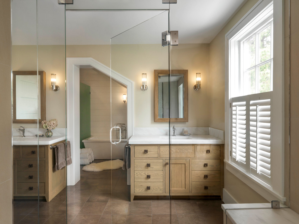 Design ideas for an expansive master wet room bathroom in Burlington with flat-panel cabinets, medium wood cabinets, a freestanding tub, beige walls, ceramic floors, an undermount sink, marble benchtops, brown floor and a hinged shower door.