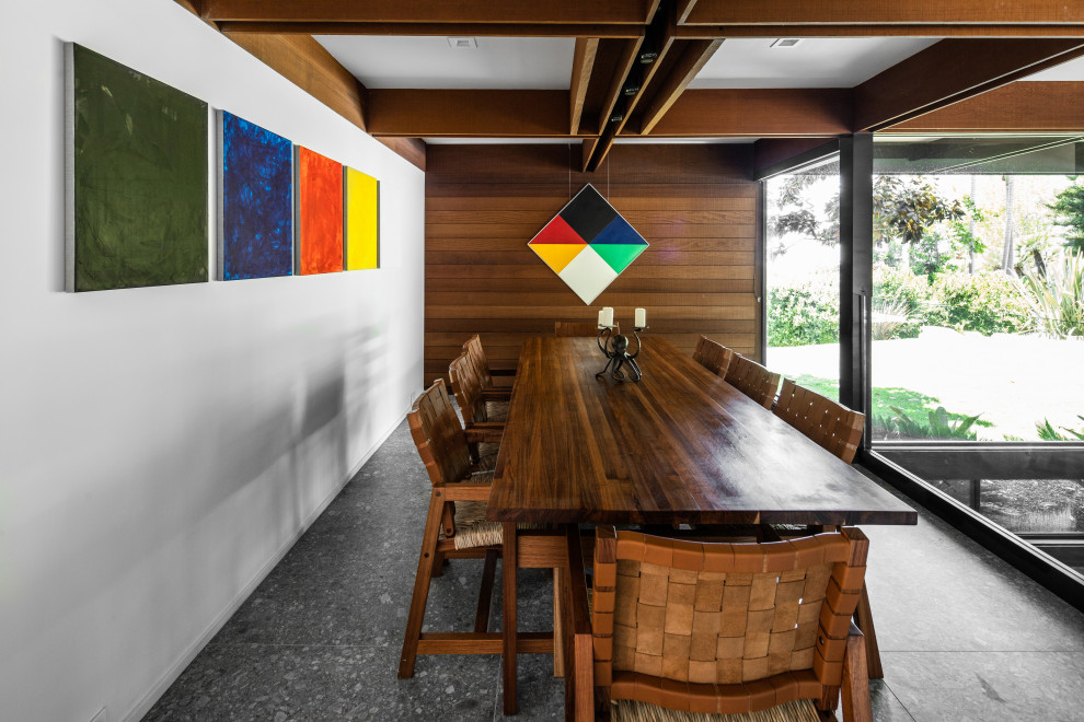 This is an example of a midcentury dining room in San Diego with white walls, grey floor, exposed beam and wood walls.