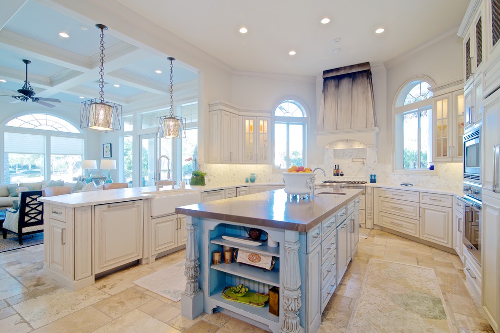 Inspiration for a mediterranean kitchen in Jacksonville with a farmhouse sink, raised-panel cabinets, marble benchtops, white splashback, mosaic tile splashback, stainless steel appliances, travertine floors and with island.