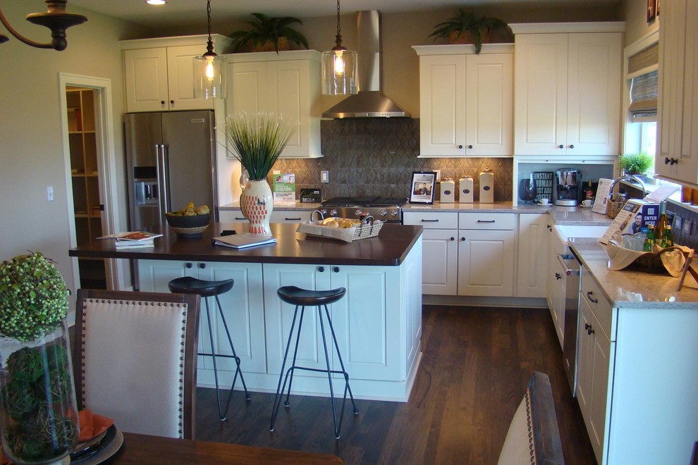 Open concept kitchen - mid-sized transitional l-shaped dark wood floor and brown floor open concept kitchen idea in Orange County with a farmhouse sink, beaded inset cabinets, beige cabinets, granite countertops, gray backsplash, porcelain backsplash, stainless steel appliances and an island