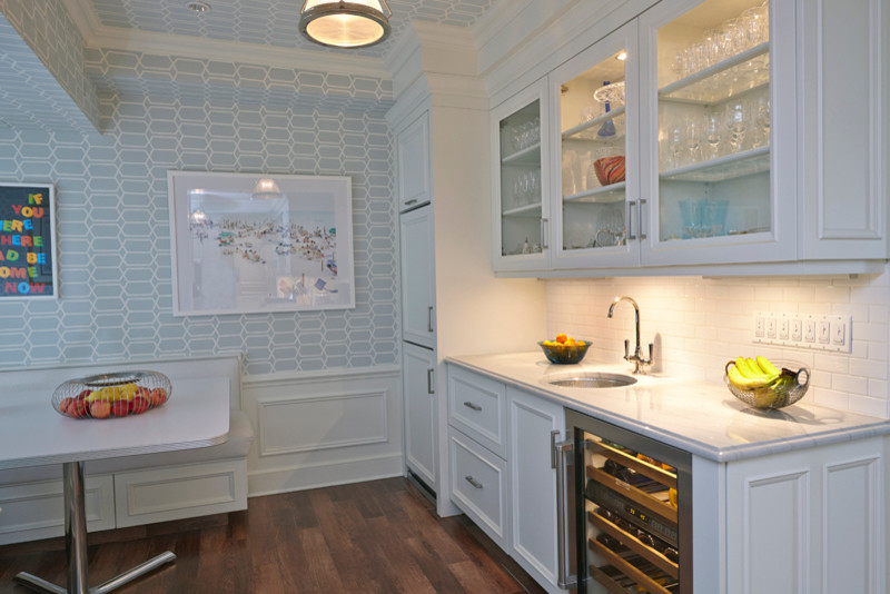 This is an example of a mid-sized transitional single-wall wet bar in New York with an undermount sink, glass-front cabinets, white cabinets, marble benchtops, white splashback, subway tile splashback, medium hardwood floors and brown floor.