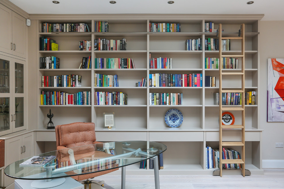 This is an example of a large transitional home office in Essex with light hardwood floors, a freestanding desk, grey floor, a library and beige walls.
