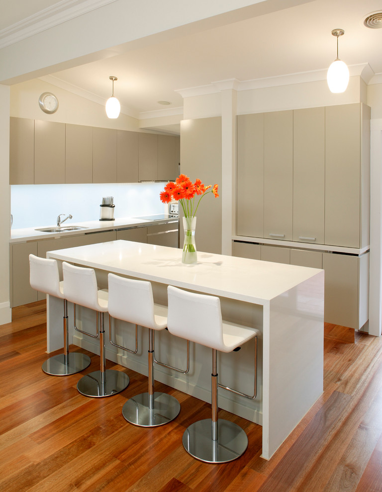 Inspiration for a mid-sized contemporary galley eat-in kitchen in Sydney with an undermount sink, flat-panel cabinets, beige cabinets, granite benchtops, white splashback, stainless steel appliances, medium hardwood floors, with island and glass sheet splashback.