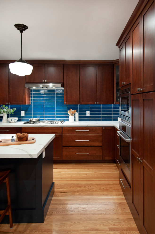 Inspiration for a large transitional l-shaped eat-in kitchen in San Francisco with a double-bowl sink, shaker cabinets, brown cabinets, blue splashback, glass tile splashback, stainless steel appliances, light hardwood floors, with island, yellow floor and white benchtop.