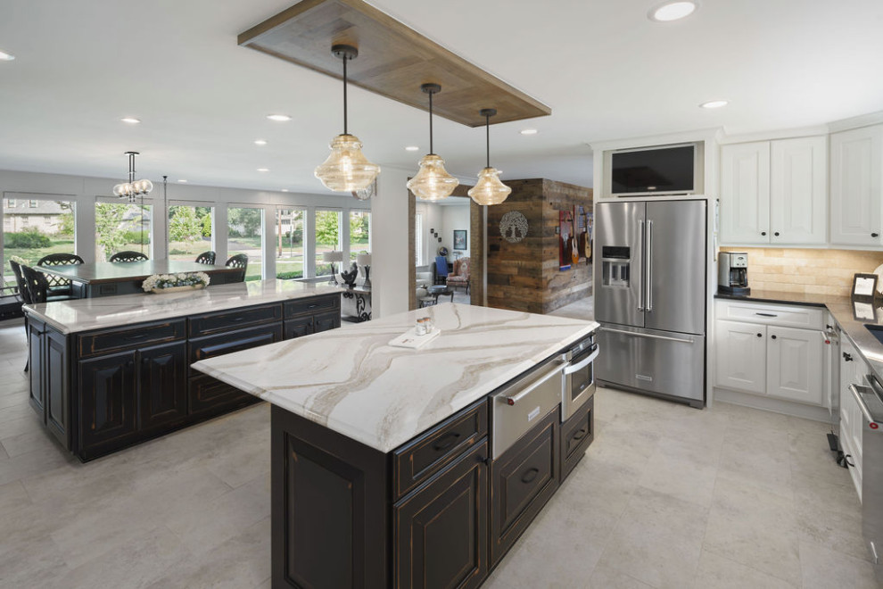 Inspiration for an expansive beach style u-shaped open plan kitchen in Columbus with a submerged sink, raised-panel cabinets, distressed cabinets, engineered stone countertops, beige splashback, travertine splashback, stainless steel appliances, travertine flooring, multiple islands, beige floors and brown worktops.
