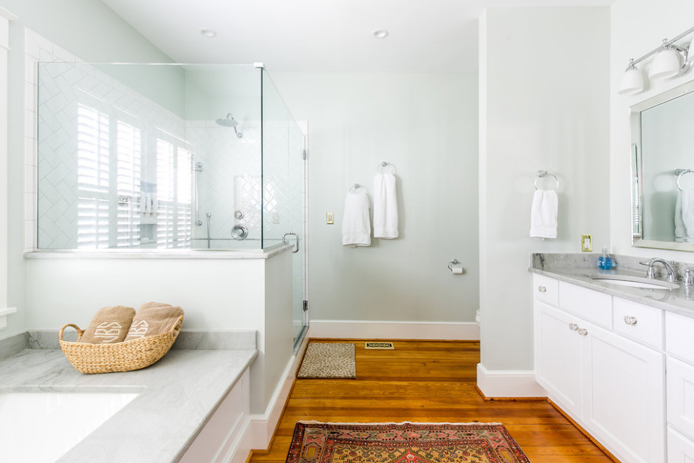 Design ideas for a medium sized traditional ensuite bathroom in Richmond with recessed-panel cabinets, white cabinets, a submerged bath, a corner shower, blue walls, medium hardwood flooring, granite worktops, brown floors, a hinged door, grey worktops, double sinks and a built in vanity unit.