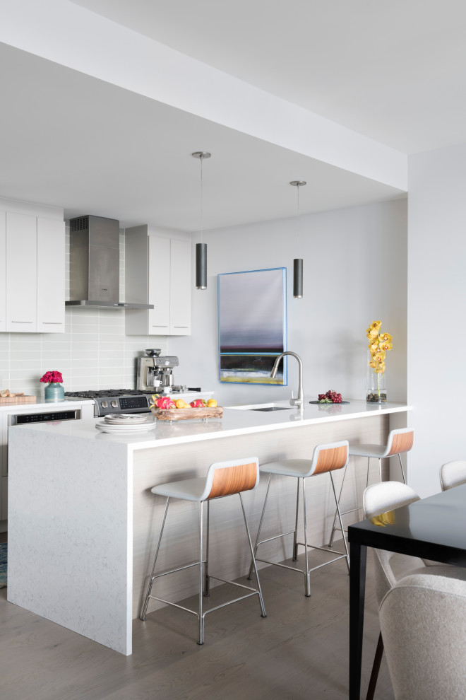 Design ideas for a small contemporary galley eat-in kitchen in Boston with flat-panel cabinets, white cabinets, quartz benchtops, grey splashback, glass tile splashback, stainless steel appliances, light hardwood floors, a peninsula, grey floor, white benchtop and an undermount sink.