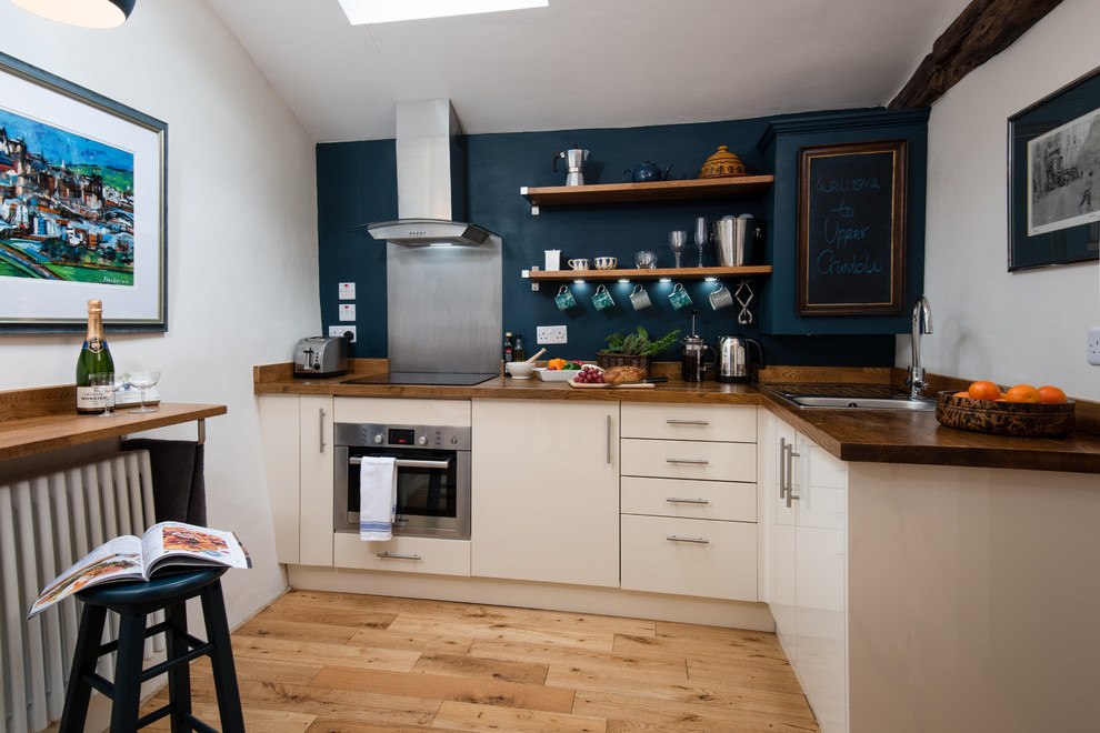 Small country l-shaped open plan kitchen in Other with a single-bowl sink, flat-panel cabinets, beige cabinets, wood benchtops, brown splashback, timber splashback, stainless steel appliances, light hardwood floors, no island, brown floor and brown benchtop.