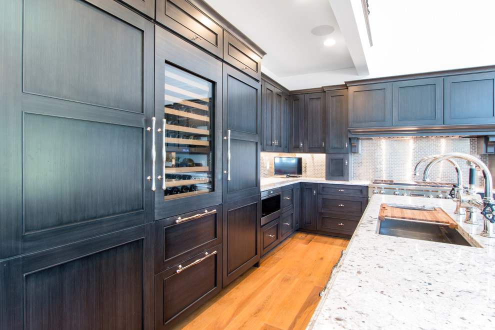 Design ideas for a large transitional l-shaped eat-in kitchen in Milwaukee with a single-bowl sink, recessed-panel cabinets, blue cabinets, granite benchtops, metallic splashback, metal splashback, panelled appliances, light hardwood floors and with island.