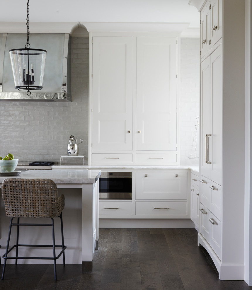 Example of a transitional medium tone wood floor and gray floor kitchen design in Chicago with an undermount sink, recessed-panel cabinets, white cabinets, quartzite countertops, white backsplash, paneled appliances, an island and white countertops