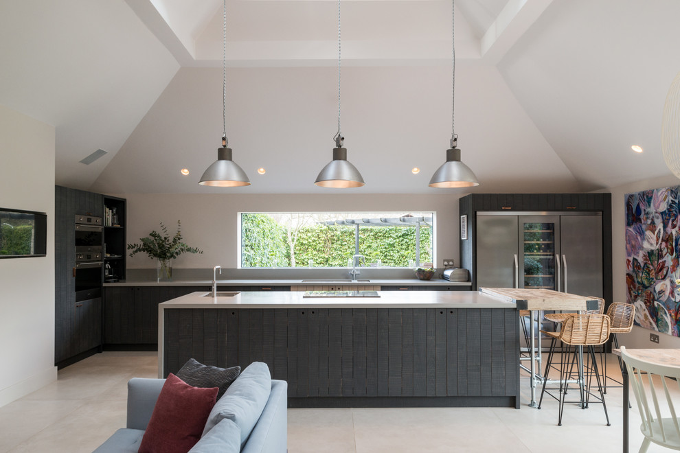 Mid-sized country l-shaped open plan kitchen in Oxfordshire with an undermount sink, beaded inset cabinets, grey cabinets, stainless steel appliances, with island, grey floor and beige benchtop.