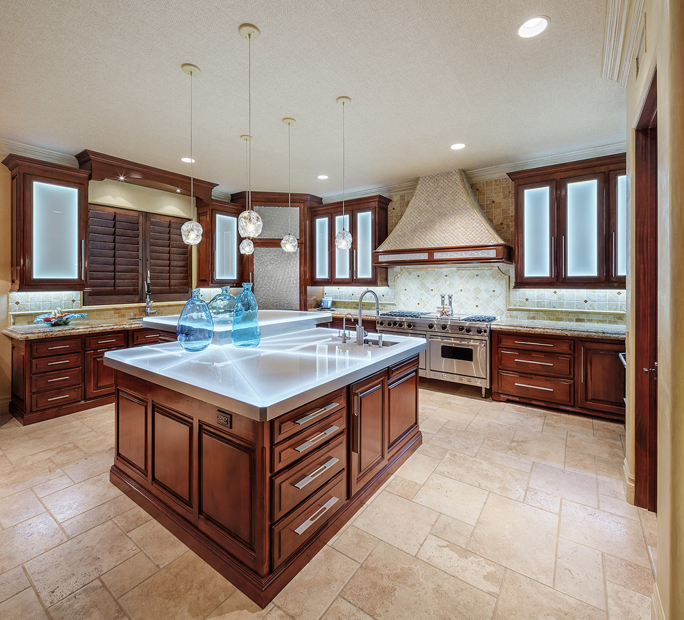 Photo of an expansive tropical l-shaped open plan kitchen in Los Angeles with an undermount sink, raised-panel cabinets, medium wood cabinets, granite benchtops, beige splashback, ceramic splashback, stainless steel appliances, travertine floors, multiple islands and beige floor.