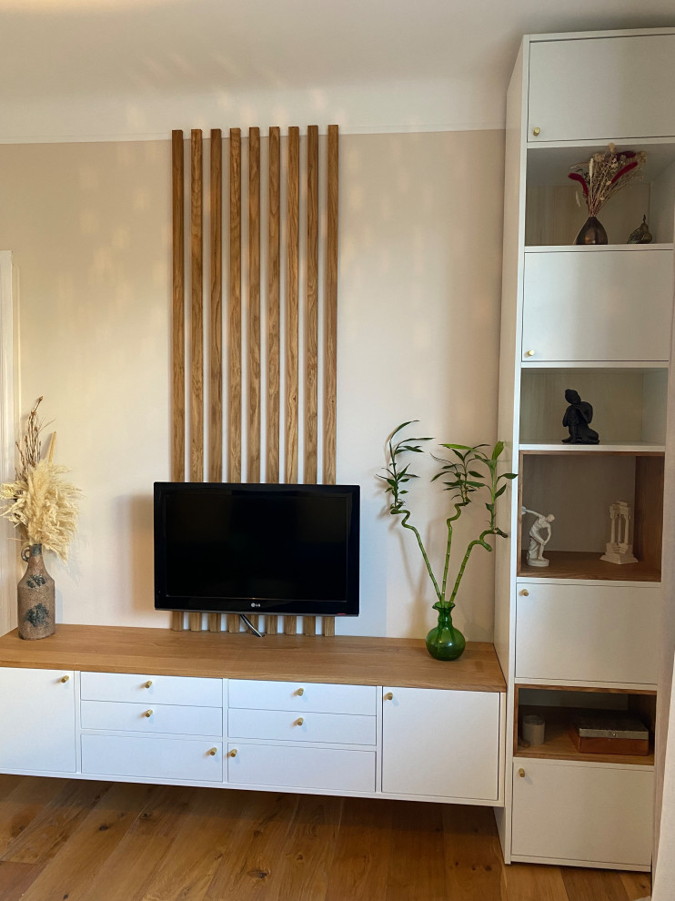Diseño de sala de estar con biblioteca abierta actual de tamaño medio sin chimenea con paredes beige, suelo de madera clara, televisor colgado en la pared y madera