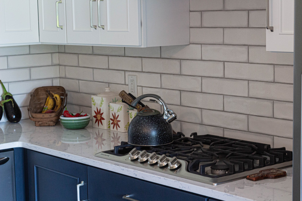 Mid-sized transitional l-shaped porcelain tile and gray floor eat-in kitchen photo with an undermount sink, flat-panel cabinets, white cabinets, quartz countertops, white backsplash, subway tile backsplash, stainless steel appliances, an island and white countertops
