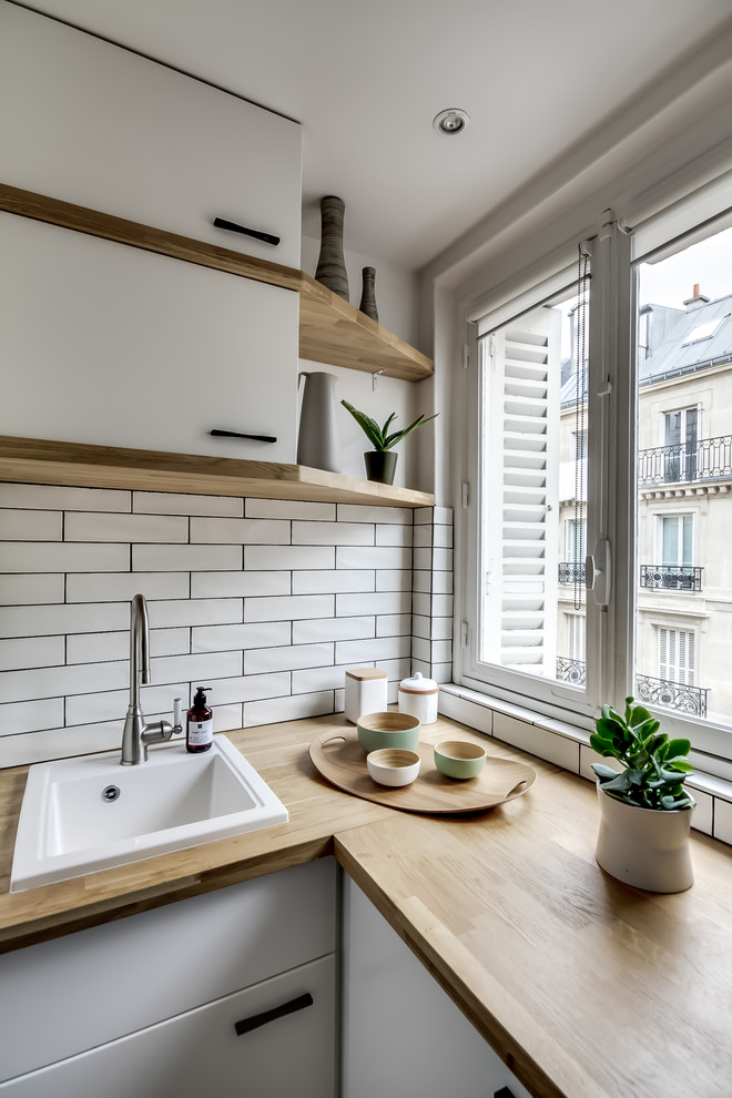 This is an example of a mid-sized scandinavian u-shaped separate kitchen in Paris with a single-bowl sink, flat-panel cabinets, white cabinets, wood benchtops, white splashback, subway tile splashback, panelled appliances, slate floors, no island, grey floor and beige benchtop.