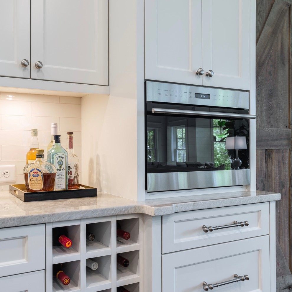Inspiration for a large transitional l-shaped medium tone wood floor eat-in kitchen remodel in Atlanta with a farmhouse sink, shaker cabinets, white cabinets, quartzite countertops, white backsplash, white appliances and two islands