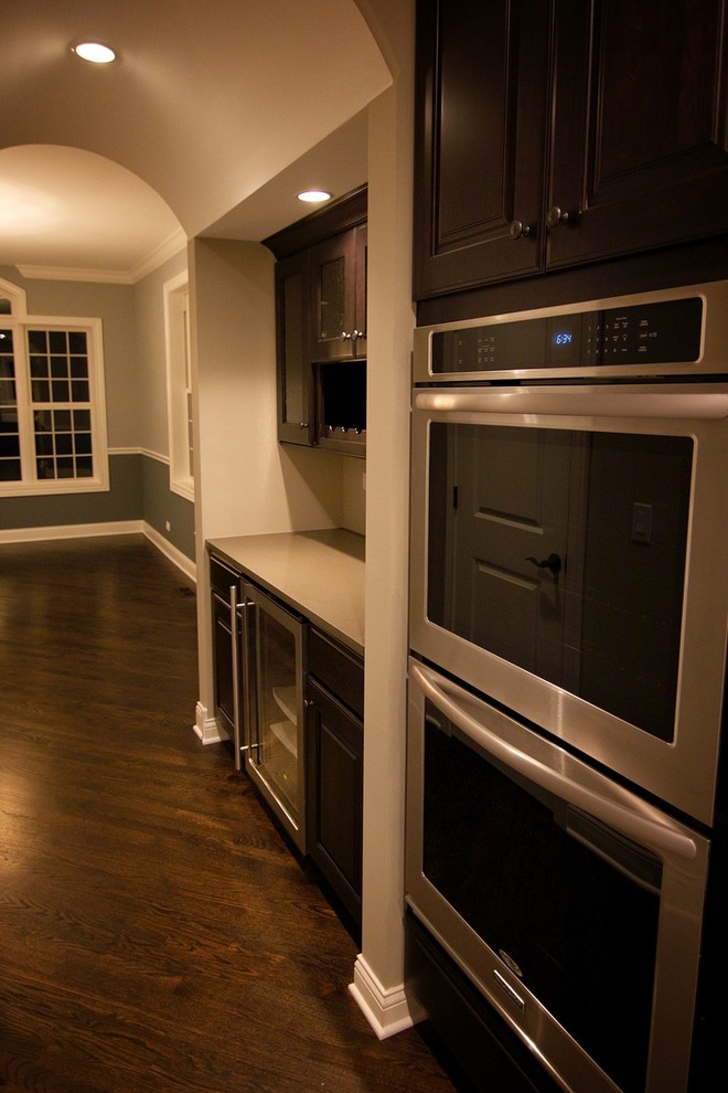 Inspiration for a mid-sized transitional single-wall dark wood floor enclosed kitchen remodel in Chicago with recessed-panel cabinets, white cabinets, solid surface countertops, white backsplash, porcelain backsplash, stainless steel appliances, an island and a farmhouse sink